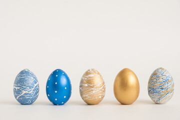 Easter golden decorated eggs stand in a row on white background. Minimal easter concept. Happy Easter card with copy space for text. Top view, flatlay.