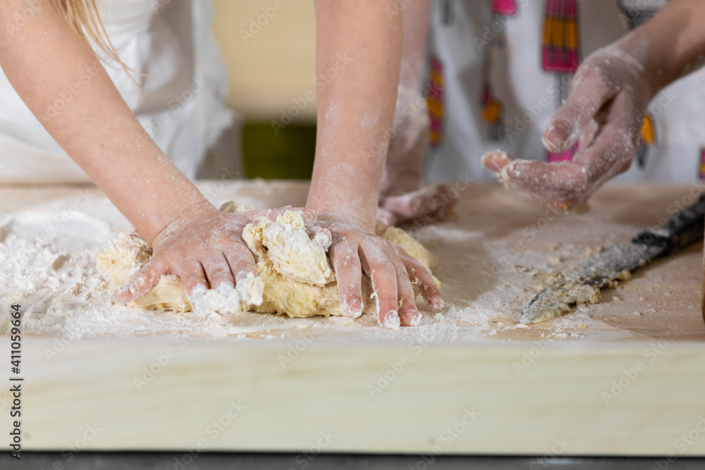 Close-up frame. In one of the last stages, mother and daughter knead and knead a cake that will serve as a pizza cake. Mother and baby do the dough together in the kitchen.