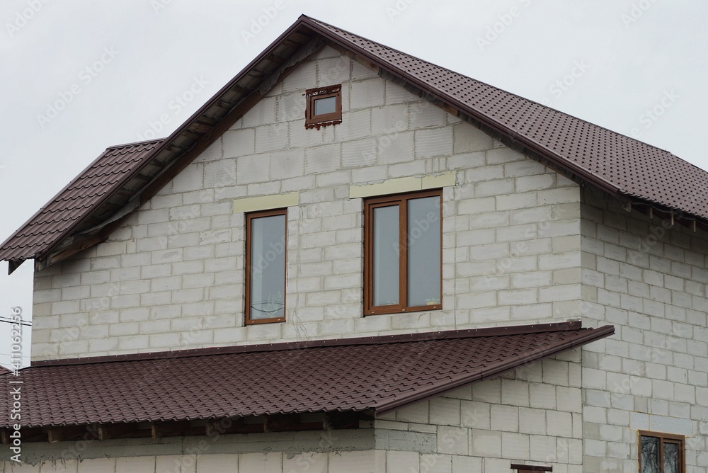 big attic of a white brick house with windows under a brown tiled roof against a gray sky