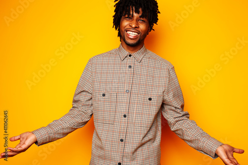 young handsome african american guy student posing cheerful and gesturing on yellow background, lifestyle people concept