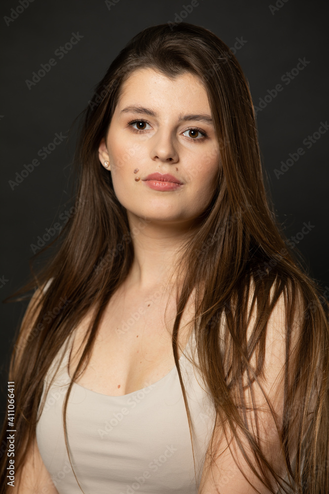 Naklejka premium Portrait of an attractive young girl who looks into the camera with beautiful long dark brown hair.