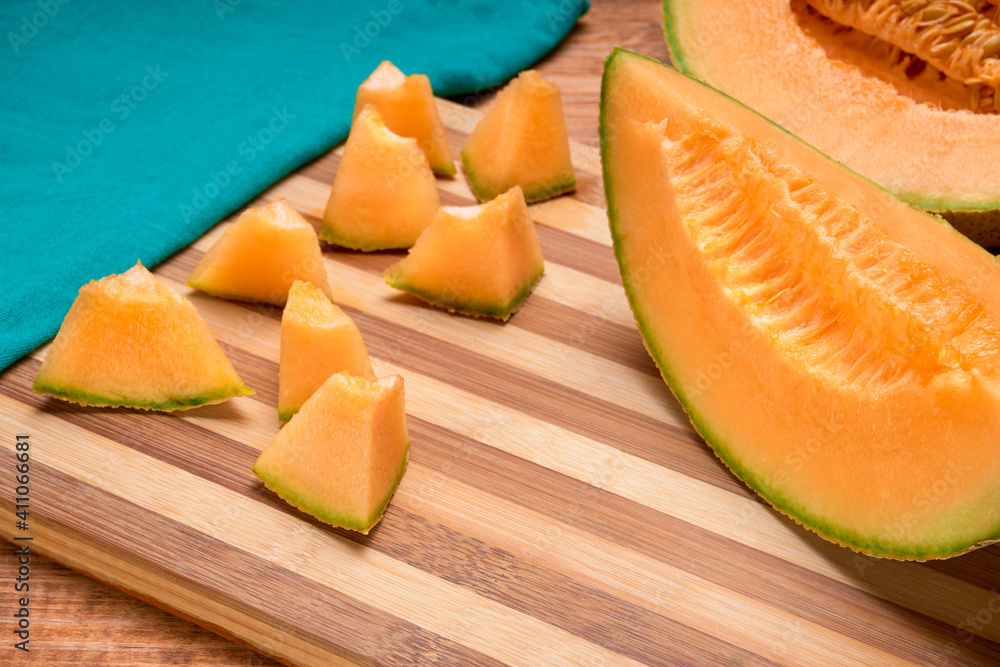 cantaloupe melon cut into small pieces on a bamboo cutting board with a green cloth napkin and a half melon on the bottom. copy space for text