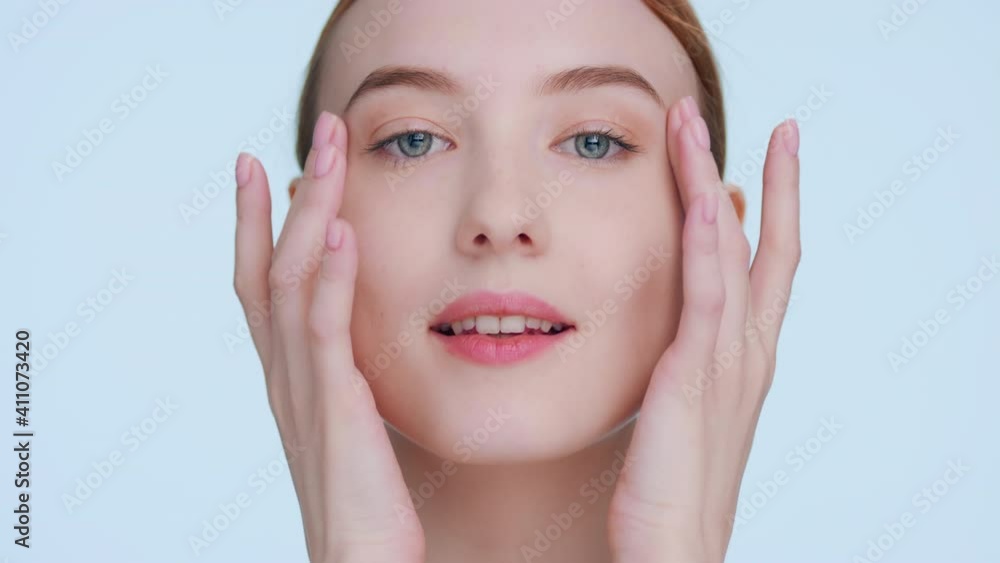 Young ginger woman touches her face runs fingers from under her eyes up to temples and down to cheeks, looks at camera and smiles | Beauty portrait and skin care products commercial shot Young ginger woman touches her face runs fingers from under her eyes up to temples and down to cheeks, looks at camera and smiles | Beauty portrait and skin care products commercial shot