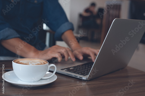 Male freelancer, casual business man online working on laptop computer with cup of coffee on wooden table in coffee shop co-working space