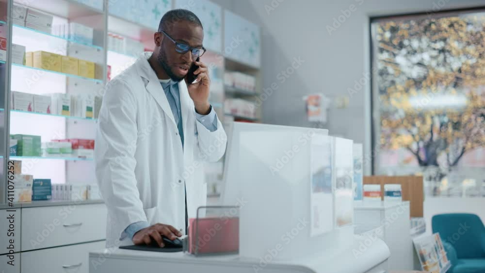 Pharmacy Drugstore Counter: Portrait of Helpful Black Male Pharmacist Talking on the Mobile Phone with Customer, Giving Medicine Recommendation, Uses Computer, Checks Prescription Drugs Availability Pharmacy Drugstore Counter: Portrait of Helpful Black Male Pharmacist Talking on the Mobile Phone with Customer, Giving Medicine Recommendation, Uses Computer, Checks Prescription Drugs Availability