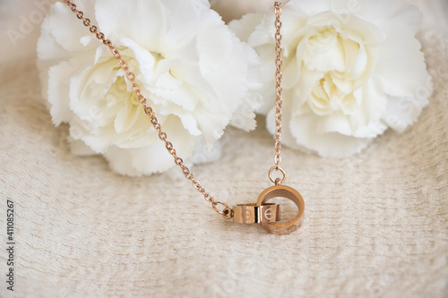 Closeup of a golden necklace with two ring pendants sitting against white carnations
