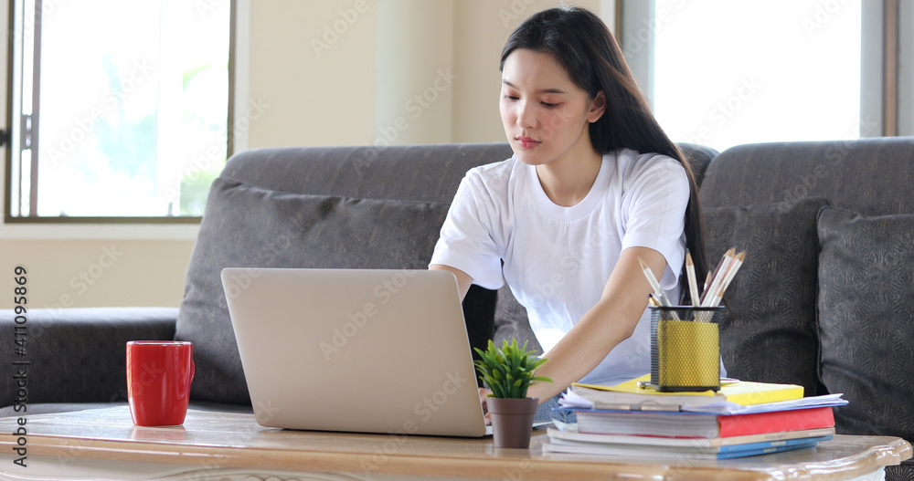 Asian woman pleased happy cheerful cute beautiful is using a notebook computer and sitting on sofa for working from home. She is quarantined at home during the coronavirus epidemic. Asian woman pleased happy cheerful cute beautiful is using a notebook computer and sitting on sofa for working from home. She is quarantined at home during the coronavirus epidemic.