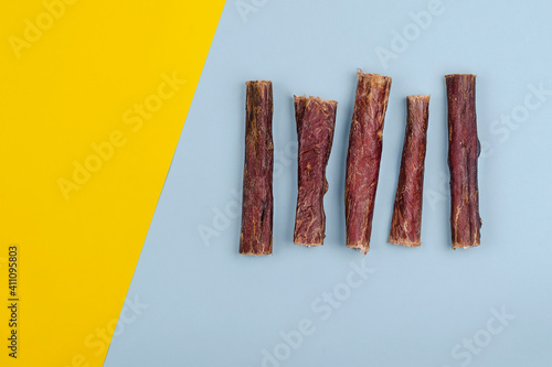 Dried natural healthy treats for dogs. Beef esophagus sticks on a yellow and blue background.