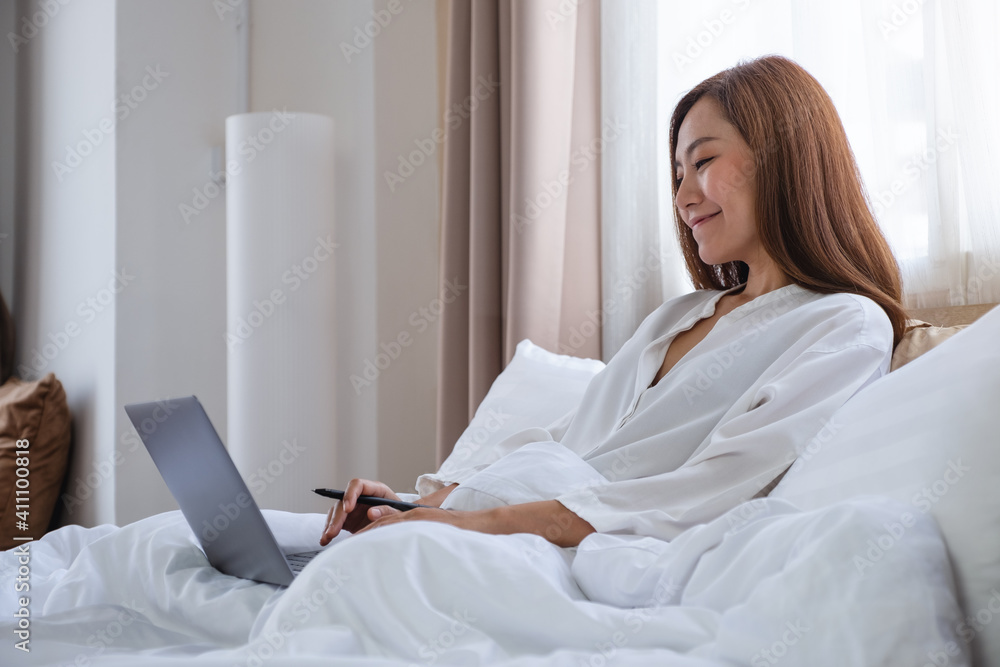 A beautiful young asian woman using and working on laptop computer while lying on bed at home A beautiful young asian woman using and working on laptop computer while lying on bed at home