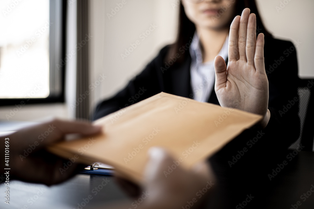 Obraz premium Businesswoman raised her hand to deny accepting a bribe from a business partner, a brown envelope containing a large number of dollar bills as money for bribery, a corruption concept.