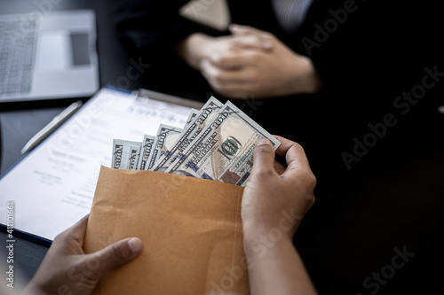 Businesswoman pulls dollar bills out of brown envelopes, hand them over to business partners as a bribe, bribery is a corrupt and illegal act. The concept of bribery.