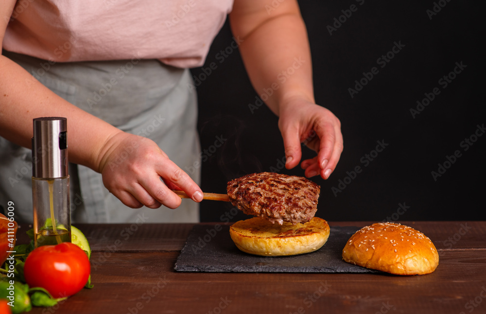 A close-up of a delicious burger being prepared. The cook puts a juicy fried cutlet on top of a toasted bun. Gastronomy, recipes, menus, fast food. Juicy burger