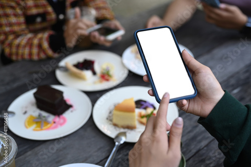 Close up view of young female using mobile phone taking photo of sweet dessert  during spending time with her friends at cafe.