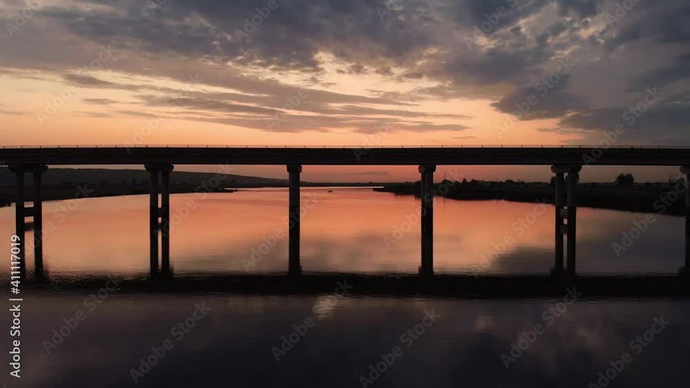 Beautiful flight under the bridge over the river at dawn. The sun is mirrored from the water surface Beautiful flight under the bridge over the river at dawn. The sun is mirrored from the water surface