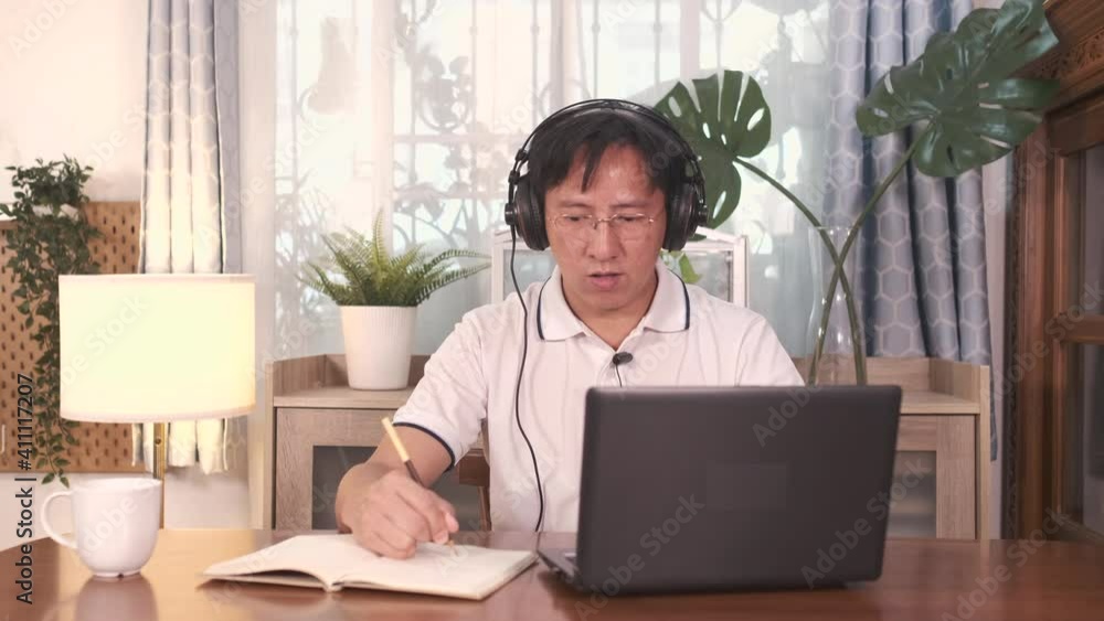 Asian business man in glasses wearing headphones with laptop computer making conference video call, attend webinar or working at home ,Work from home, technology and people concept Asian business man in glasses wearing headphones with laptop computer making conference video call, attend webinar or working at home ,Work from home, technology and people concept
