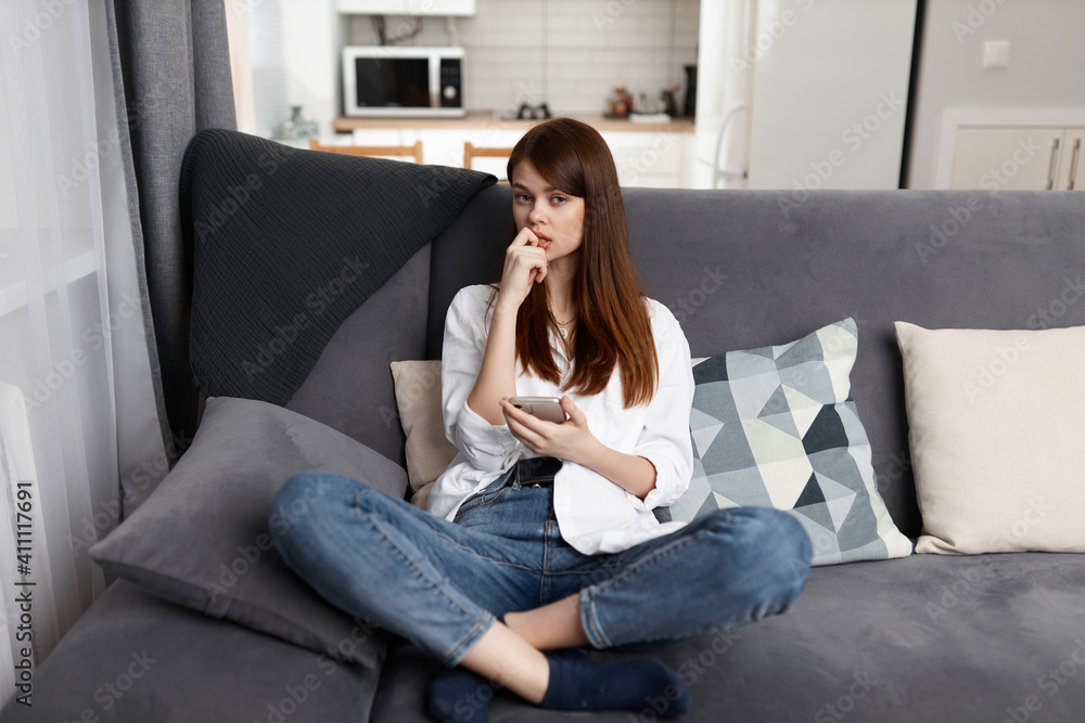 Fototapeta premium pretty woman with a phone in her hands at home on a comfortable sofa chatting