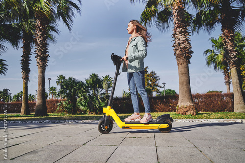 Young casual modern active millennial woman using electric scooter for fast mobile riding through the city