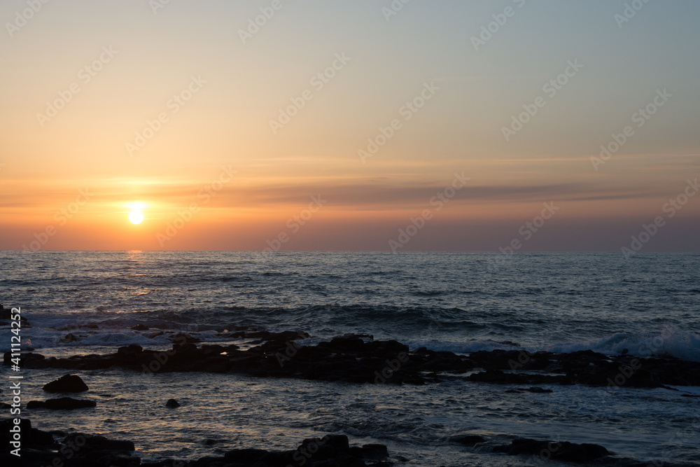 水平線に沈む夕陽と岩の海岸
