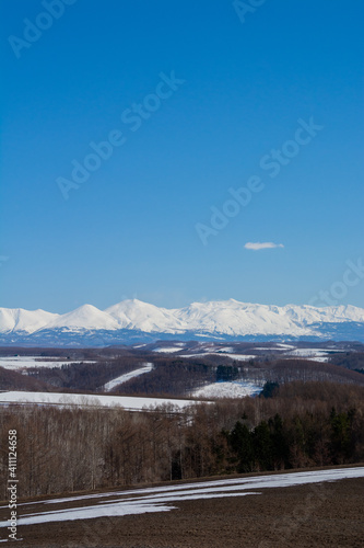 春の残雪の畑と雪山　十勝岳連峰  © kinpouge