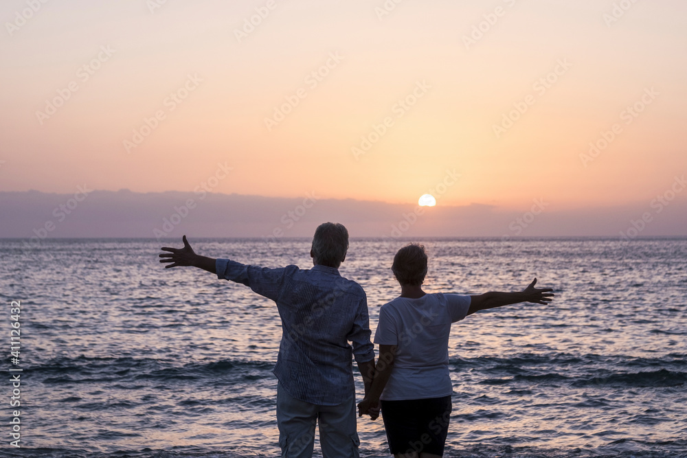 Happy senior couple people in love enjoy a sunset on the ocean holding hands - ñpve and relationship elderly summer holiday lifestyle man and woman together in happiness looking the sea