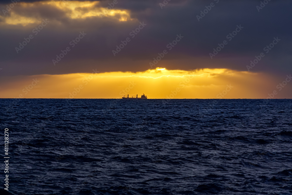 Freighter ship in the distance above the sea horizon on a sunset with dramatic sky. Gran Canaria. Spain