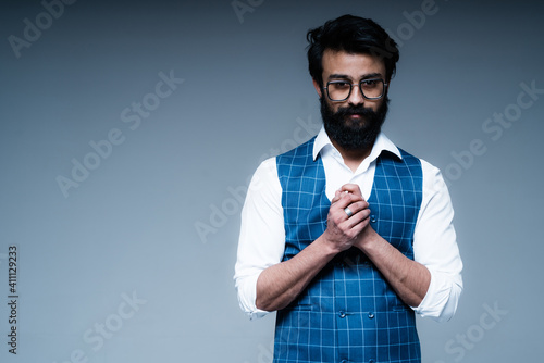 Stylish businessman in a white shirt with black hair and a beard stands with his palms together