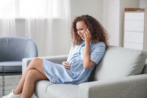 Stressed pregnant African-American woman talking by mobile phone at home