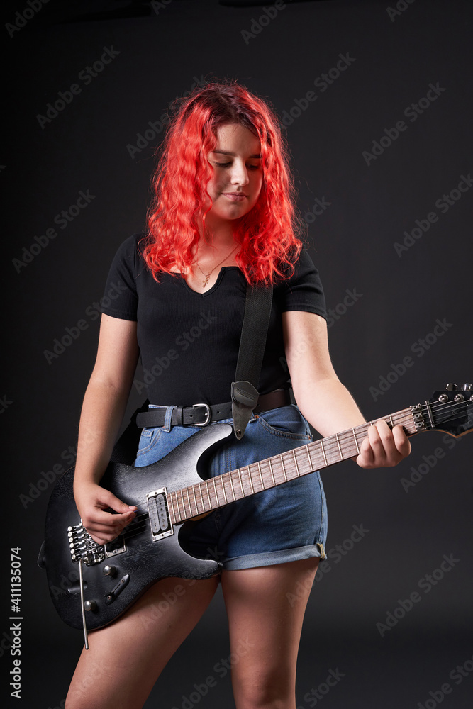Teenager girl with red hair plays the electric guitar on a black background