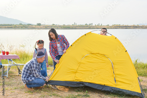 Asian parent with children setting tent by the lake. Family outdoor activity adventure on vacation.