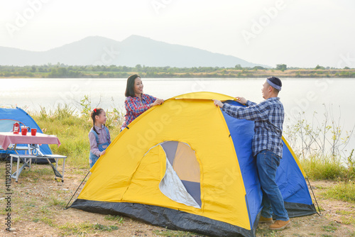 Asian parent with daughter setting tent by the lake. Family outdoor activity adventure on vacation.