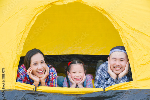 Happy asian family camping on vacation .Father, mother and daughter lying together in tent and smile.