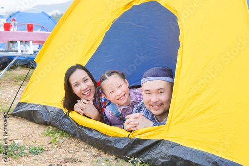 Happy asian family camping on vacation .Father, mother and daughter lying together in tent and smile.