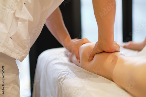 Detail of hands massaging human calf muscle.Therapist applying pressure on female leg. Hands of massage therapist massaging legs of young woman in spa salon. Body care in spa salon for young woman.