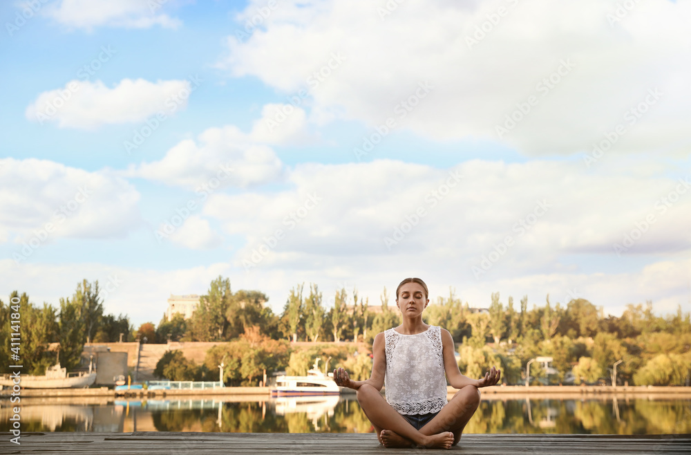 Young woman meditating near river at sunset, space for text. Nature healing power