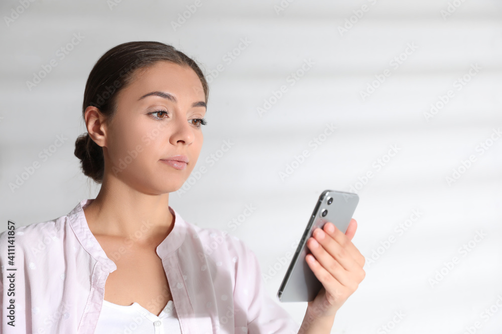 Young woman unlocking smartphone with facial scanner near white wall. Biometric verification Young woman unlocking smartphone with facial scanner near white wall. Biometric verification