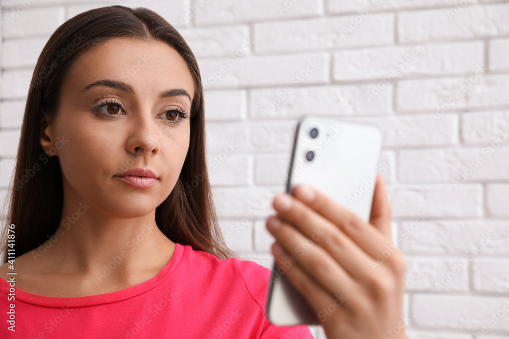 Young woman unlocking smartphone with facial scanner near white brick wall. Biometric verification Young woman unlocking smartphone with facial scanner near white brick wall. Biometric verification
