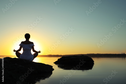 Woman practicing yoga near river on sunset. Healing concept © New Africa