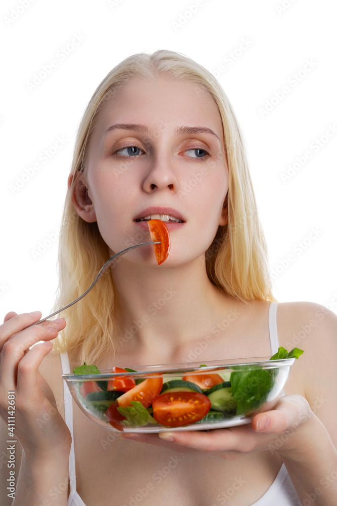 Good looking woman eating a bowl of salad while standing against a white background Good looking woman eating a bowl of salad while standing against a white background