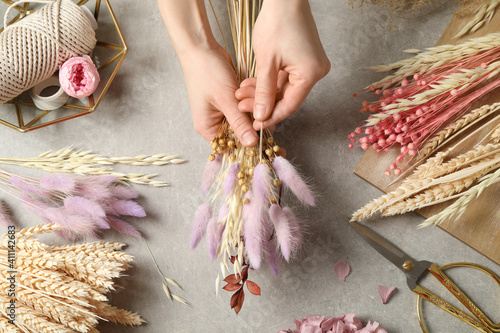 Fototapeta Naklejka Na Ścianę i Meble -  Florist making bouquet of dried flowers at grey stone table, top view