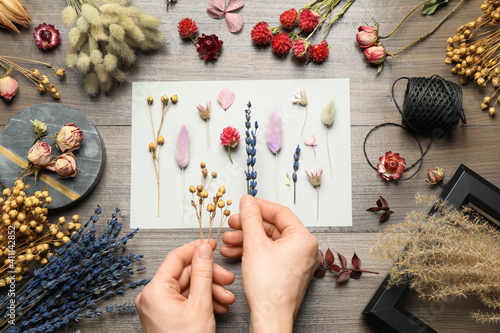 Woman making herbarium of dry flowers at wooden table, closeup