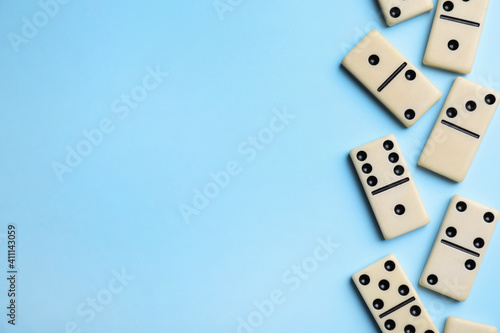Classic domino tiles on light blue background  flat lay. Space for text