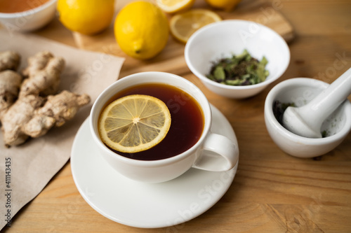 A white cup of green natural tea with ginger, lemon and honey on wooden rustic background.