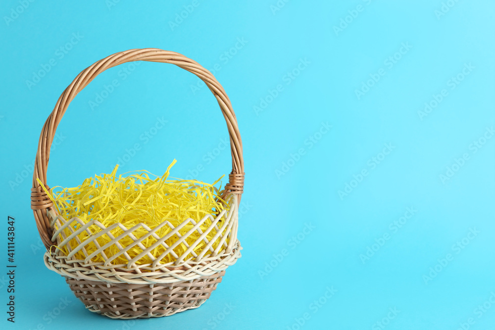 Easter basket with yellow paper filler on light blue background, space for text