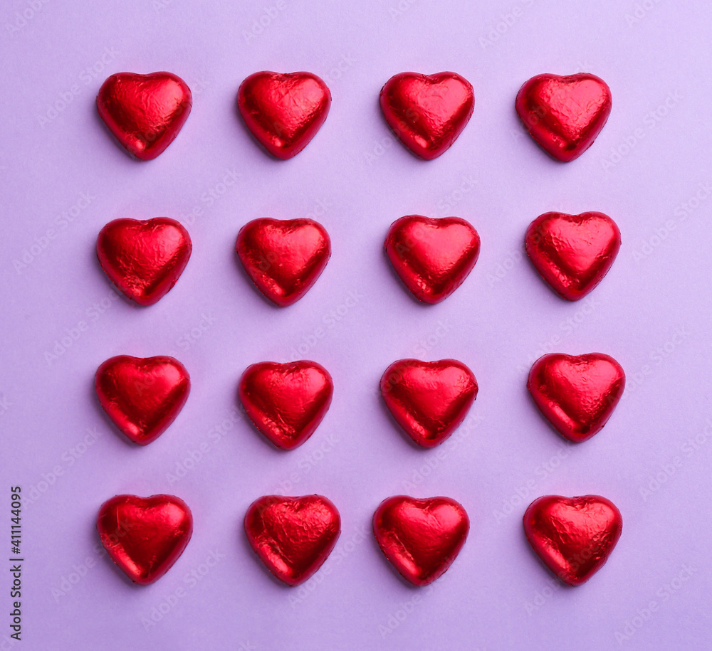 Heart shaped chocolate candies in red foil on violet background, flat lay