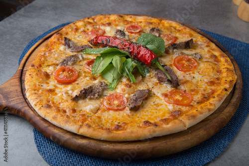 Pizza with sausage, cheese, baby corn, rocket leaves and roasted red pepper on wooden pizza plate 