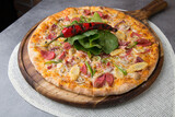 Pizza with sausage, cheese, baby corn, rocket leaves and roasted red pepper on wooden pizza plate 