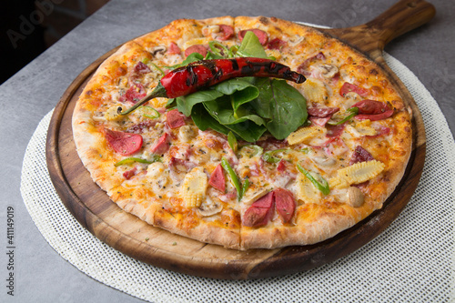 Pizza with sausage, cheese, baby corn, rocket leaves and roasted red pepper on wooden pizza plate 