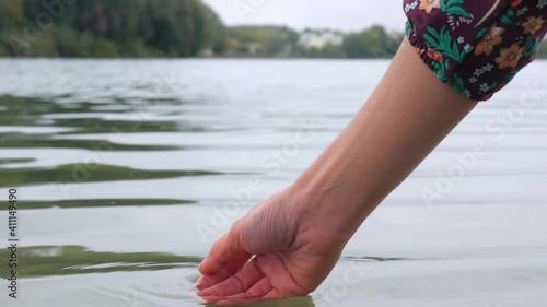 The girl touches the water on the river with her fingers. Close-up shot of a woman's hand on a background of water by the lake. photo