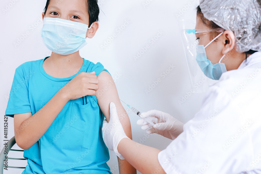 A boy patient wearing a mask with a happy expression when being injected by the doctor, vaccination coronavirus campaign. Medicine, vaccination, immunization and health care concept A boy patient wearing a mask with a happy expression when being injected by the doctor, vaccination coronavirus campaign. Medicine, vaccination, immunization and health care concept
