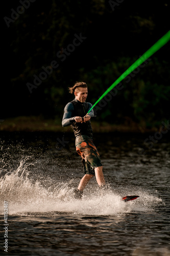 man holds bright green cable and rides down the river on wakeboard. © fesenko